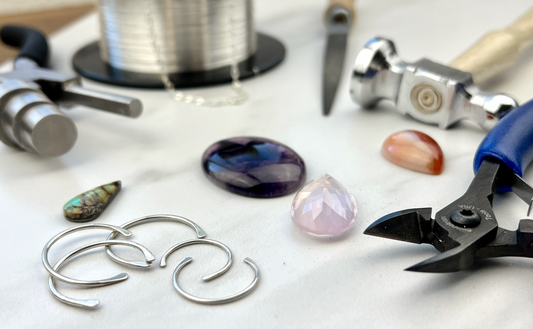 a white table full of tools, wire, silver, and gemstones